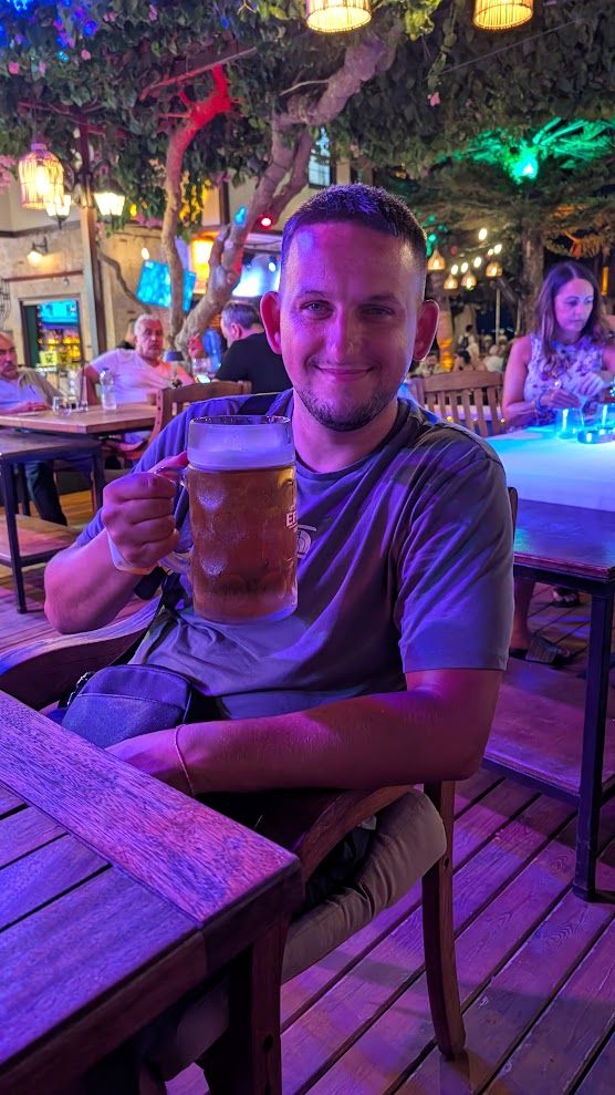 Alex smiling and raising a pint of beer at an outdoor bar